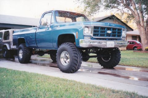 1989 Ford Bronco - This lifted blue pickup truck features large off-road tires and a prominent grille. A second vehicle is visible to the left, and a small re…