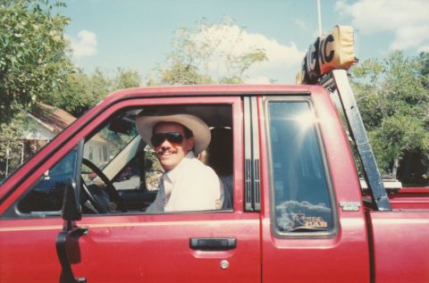 1989 Ford Bronco - Man wearing a cowboy hat sits in the driver's seat of a red Toyota pickup truck.