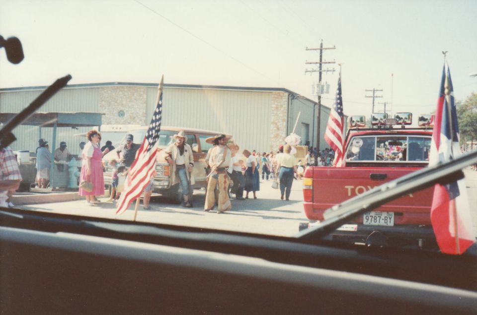 Parade scene with people in cowboy outfits, American flags, and a red Toyota truck