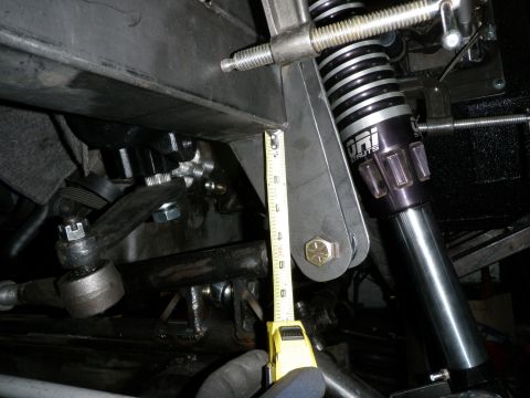 1961 International Scout 800 - Close-up of vehicle suspension components, including a shock absorber and steering linkage, with a tape measure indicating measurement.