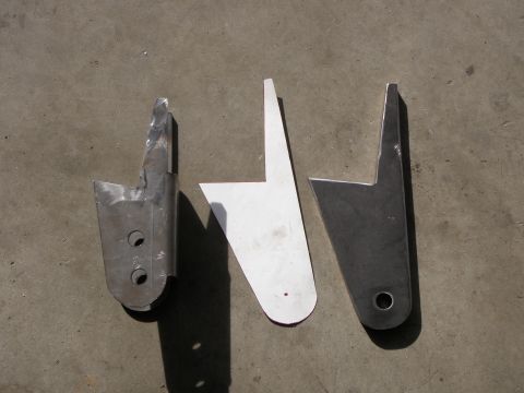 1961 International Scout 800 - Three metal brackets are laid out on a concrete surface, showing variations in finish and condition.