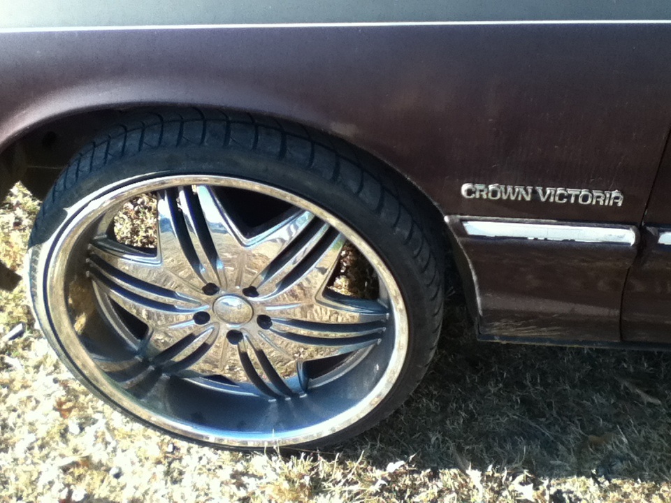Close-up of a Crown Victoria's front wheel with aftermarket rims. The car is dark brown