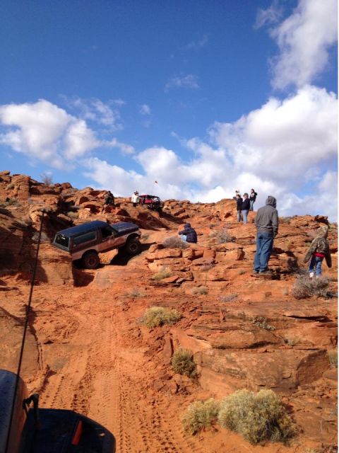 1994 Ford Bronco - Several off-road vehicles, including a 1994 Ford Bronco, tackle a challenging rocky incline under a blue sky.