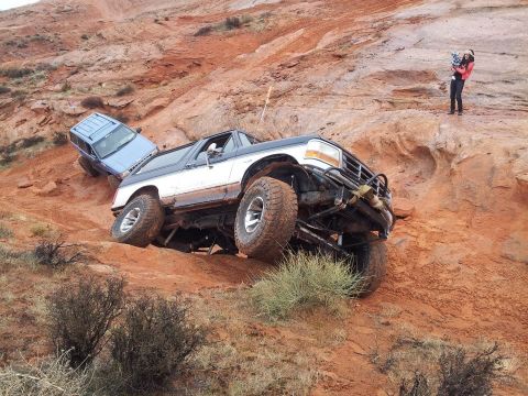 1994 Ford Bronco - A lifted, mud-covered Ford Bronco navigates a steep, rocky trail with another SUV behind it.