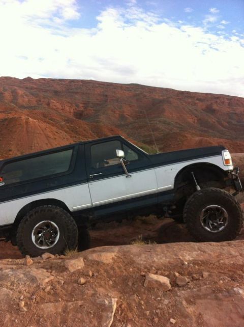 1994 Ford Bronco - This lifted SUV navigates rocky terrain under a cloudy sky.