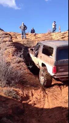 1994 Ford Bronco - 1994 Ford Bronco tackling a challenging off-road trail in a desert landscape.