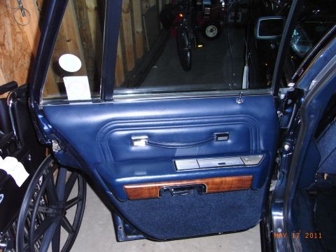 1991 Ford LTD Crown Victoria - The interior door panel of a vehicle, blue upholstery, wood trim, and chrome accents. A wheelchair is visible to the left.
