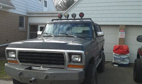 1979 Ford Bronco - A dark blue 1978 Ford Bronco is parked in front of a garage, equipped with a custom bumper and skull-themed roof lights.