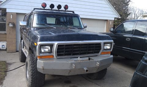 1979 Ford Bronco - Front view of a lifted 1979 Ford Bronco with aftermarket lights and bumper, parked next to another vehicle.