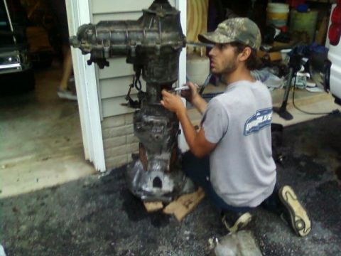 1995 Ford Bronco - A man works on a large transmission and transfer case assembly outdoors.