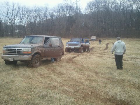 1995 Ford Bronco - Muddy 1995 Ford Bronco being towed in a field with other vehicles and people present.