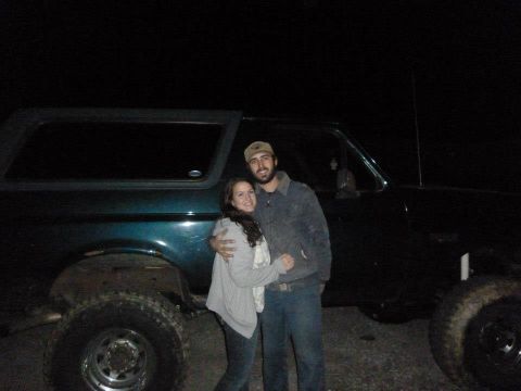1995 Ford Bronco - A couple poses in front of a dark green 1995 Ford Bronco.