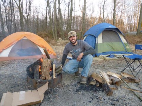 1995 Ford Bronco - Man enjoys a campfire while camping with tents set up in a wooded area.