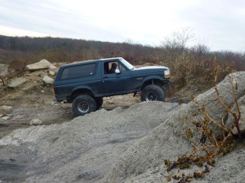 1995 Ford Bronco - This SUV is shown off-roading on a challenging rocky incline under an overcast sky.