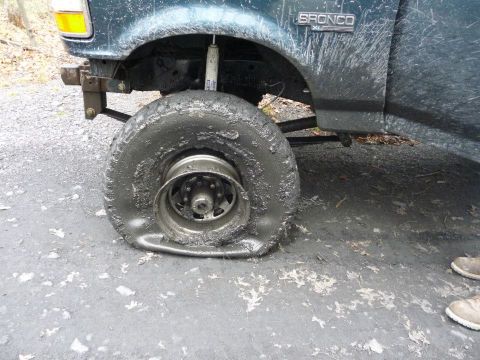 1995 Ford Bronco - A green Ford Bronco with a flat tire sits on a muddy surface, showing the front fender and wheel.