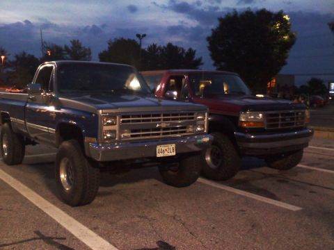 1995 Ford Bronco - A red Ford F-150 truck is parked next to a blue Chevrolet pickup truck.