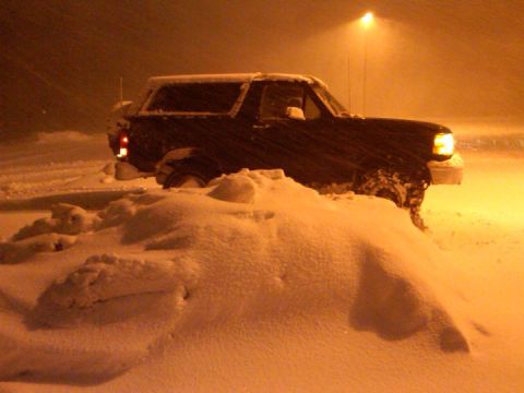 1995 Ford Bronco - A 1995 Ford Bronco is partially buried in snow, its headlights cutting through the blizzard.