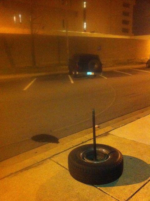 1995 Ford Bronco - A spare tire rests on the curb at night, with a dark SUV parked in the background.