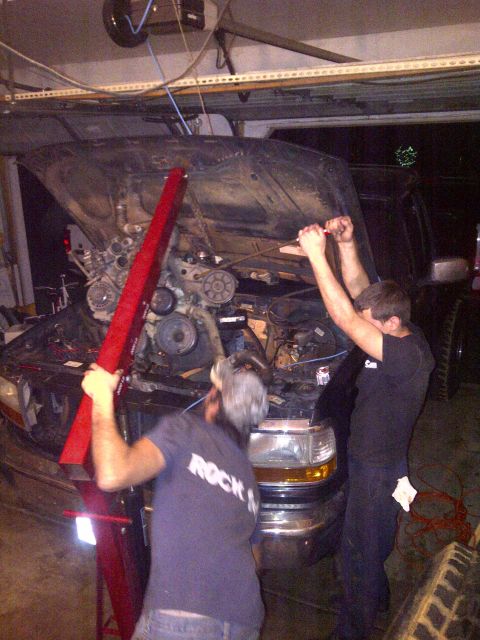 1995 Ford Bronco - Mechanics are in the process of removing the engine from a vehicle in a garage setting.