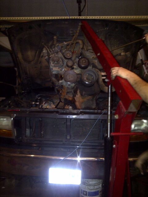 1995 Ford Bronco - Engine hoist is actively removing a V8 engine from a vehicle's engine bay.