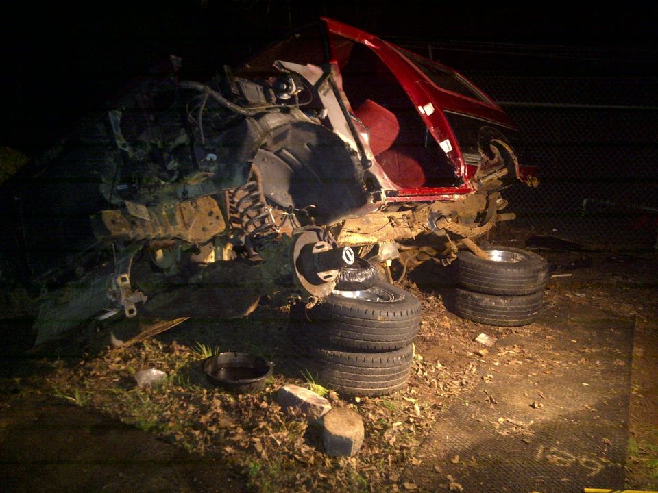 wrecked red SUV, front end missing, wheels stacked nearby
