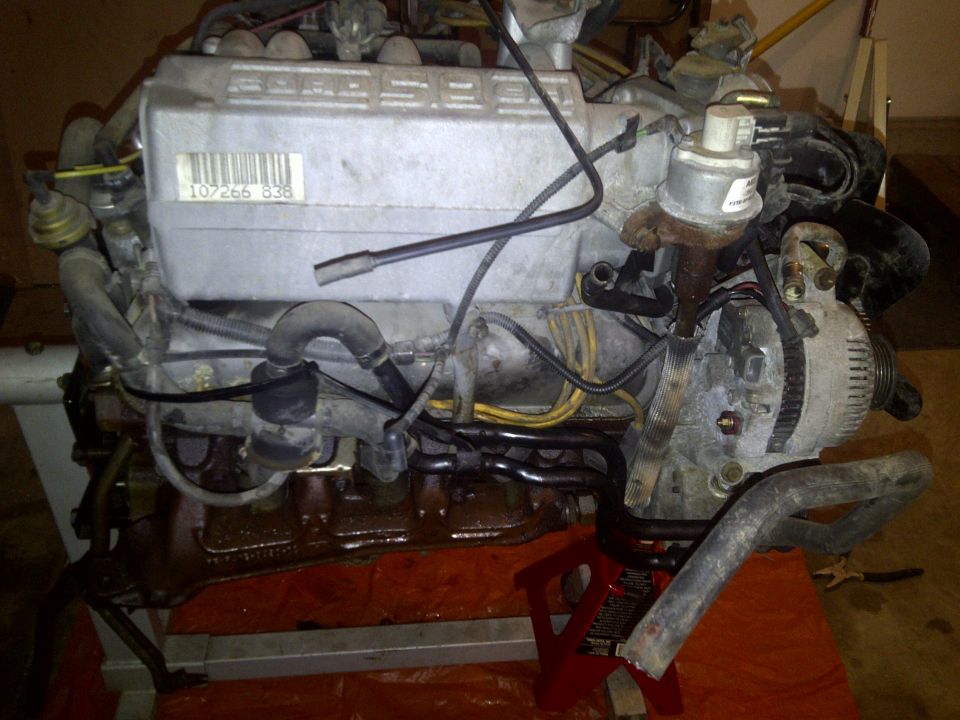 Engine on red jack stands, showing intake manifold with barcode and alternator