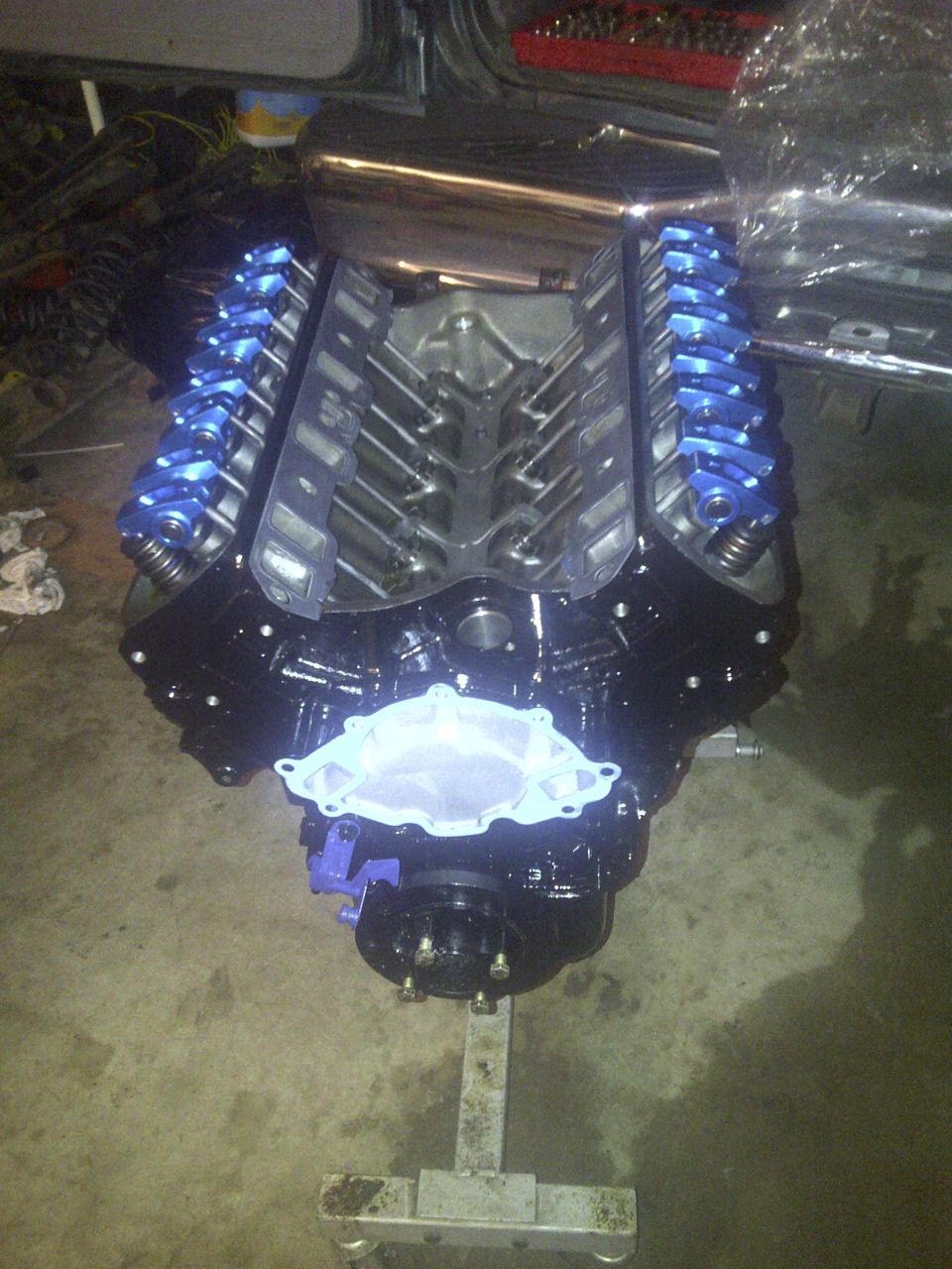 Black V8 engine with blue valve covers on an engine stand, showing intake manifold gasket