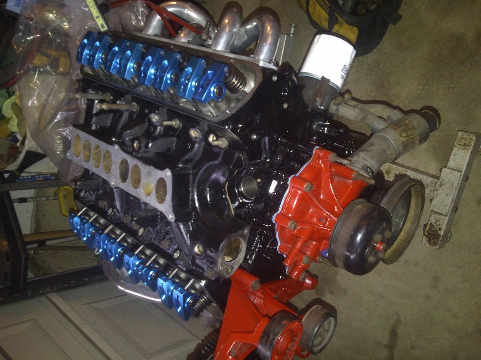 Black V8 engine with blue valve covers and red water pump, angled view