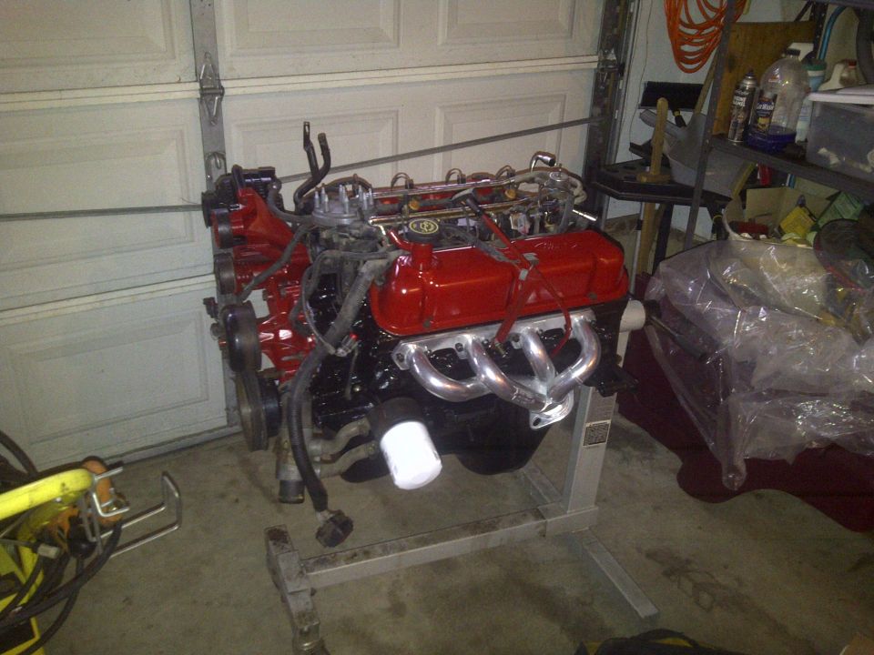 V8 engine with red valve covers and chrome headers on an engine stand