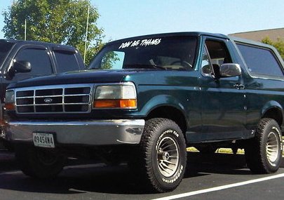 1995 Ford Bronco - A green 1995 Ford Bronco is parked next to another vehicle under a clear sky.