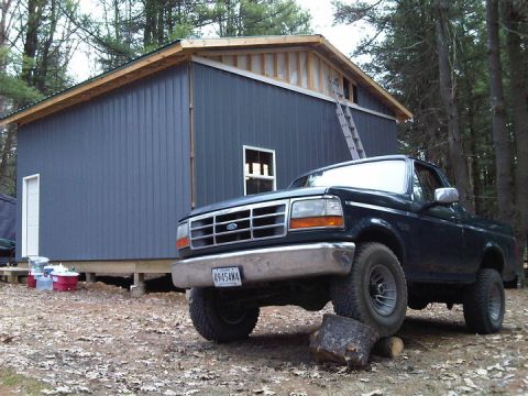 1995 Ford Bronco - A dark 1995 Ford Bronco is parked in front of a blue building with a ladder leaning against it.