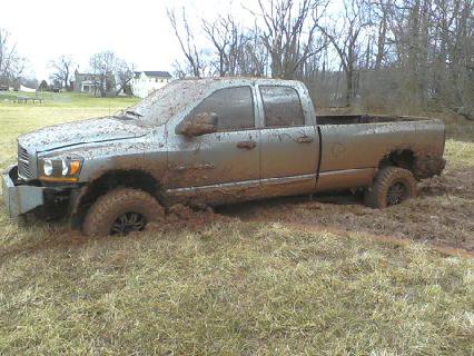 1995 Ford Bronco - A light-colored pickup truck is deeply stuck in mud, with its tires submerged and body splattered with dirt.