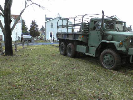 1995 Ford Bronco - A large green military truck is parked on a grassy area next to houses, with another vehicle in the distance.