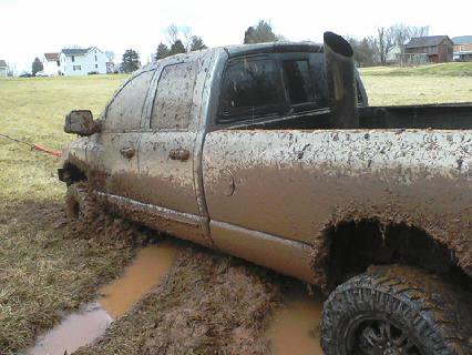1995 Ford Bronco - This pickup truck is deeply stuck in mud, with its tires submerged and body covered in dirt.