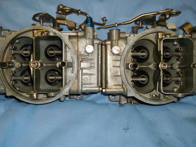 Two silver carburetors with visible linkages and blue fitting, resting on a blue cloth