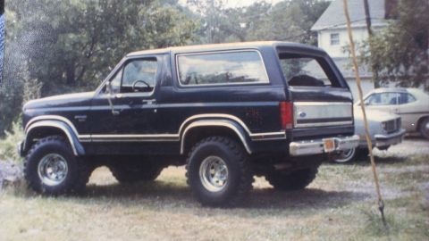 1995 Ford Bronco - A dark-colored Ford Bronco is parked in a grassy area next to another vehicle.