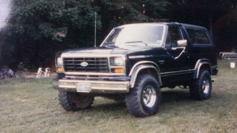 1995 Ford Bronco - This black Ford Bronco is parked on a grassy lawn with trees in the background.