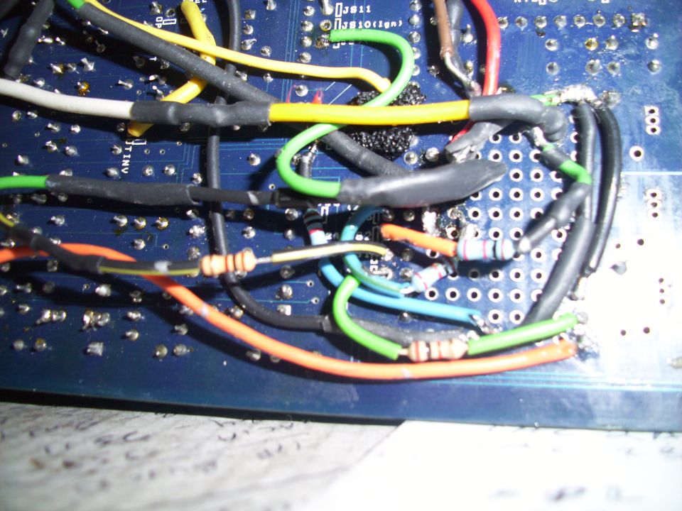 Close-up of a blue circuit board with many wires and resistors soldered on