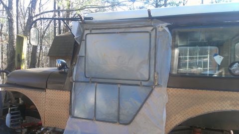 1978 Ford Bronco - A 1978 Ford Bronco's side is partially covered in plastic sheeting, revealing a custom door frame and diamond plate fender.