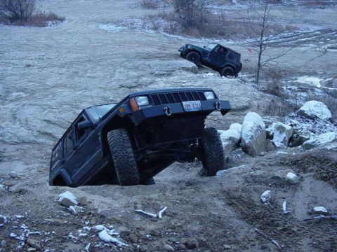 1992 Ford Bronco - Off-road vehicles navigate a challenging, uneven terrain with scattered rocks and patches of snow.