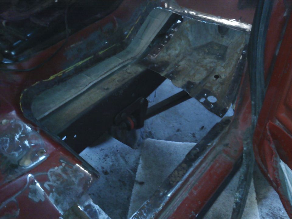 Interior floor pan of a vehicle undergoing repair, showing cut metal and exposed structure