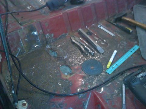 1978 Ford Bronco - Tools and a cutting disc are laid out on the rusty interior floor of a vehicle.