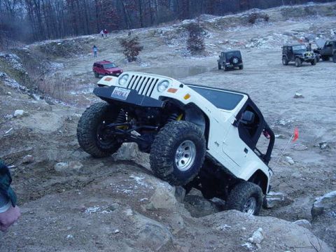 1992 Ford Bronco - A white Jeep Wrangler navigates a challenging off-road course with other vehicles present.