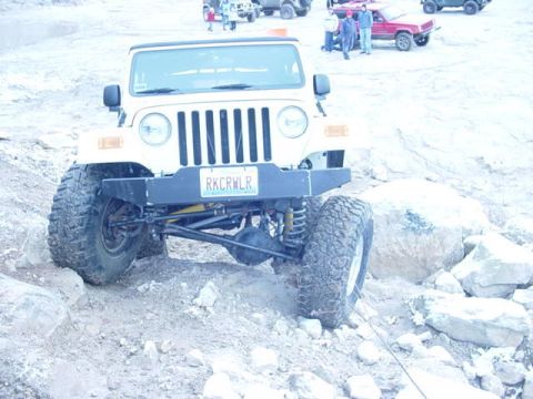 1992 Ford Bronco - A white Jeep Wrangler navigates a rocky trail with other vehicles visible in the background.