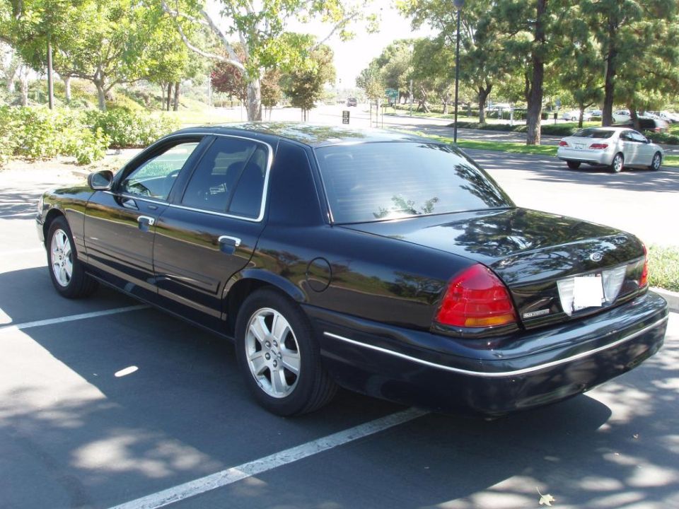 Black 2003 Ford Crown Victoria parked in a lot, side and rear view. Another car is in the background