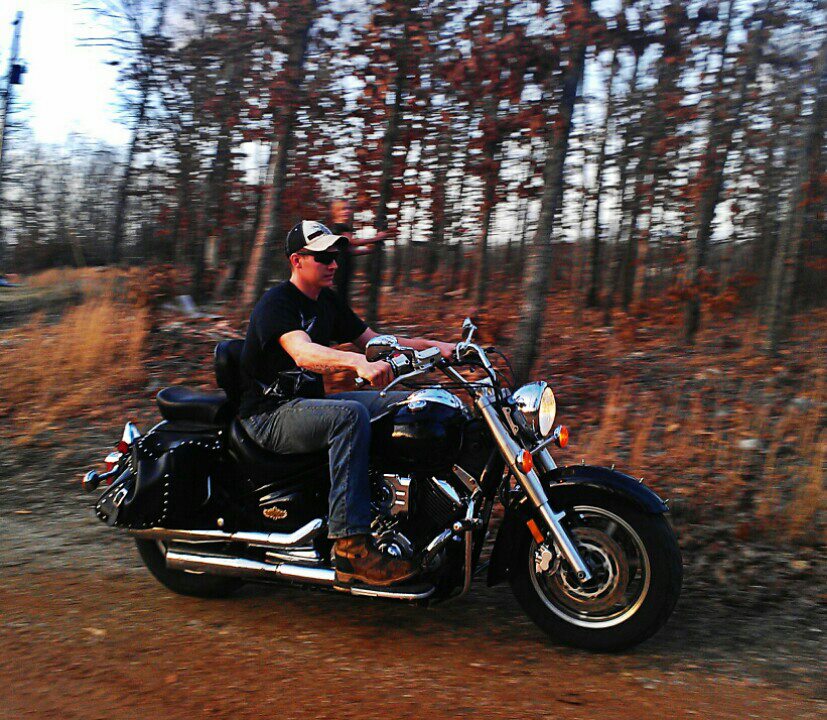 guy riding a black motorcycle on a dirt road through trees
