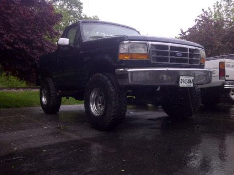 1995 Ford Bronco - A dark blue 1995 Ford Bronco is parked on a wet surface, showing its front three-quarter view and lifted stance.