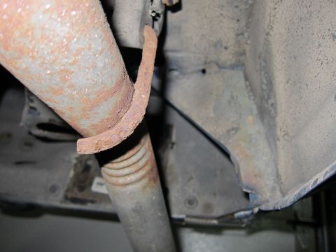 1991 Ford LTD Crown Victoria - Close-up view of rusted exhaust system and suspension components underneath a vehicle.