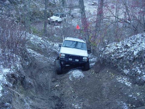 1992 Ford Bronco - Two Jeep Cherokees navigate a challenging off-road trail in a wooded, snowy environment.