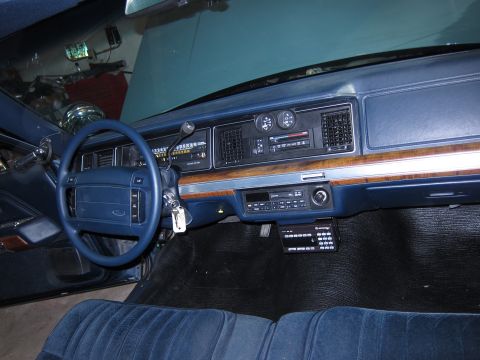 1991 Ford LTD Crown Victoria - The interior of a car features a blue dashboard, steering wheel, and velour seats, with a radio and a mounted keypad visible.